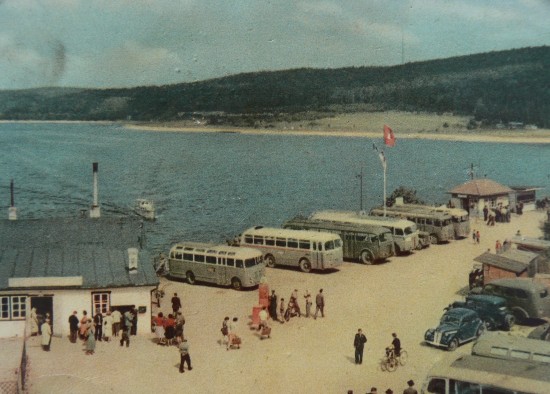 Kolorované pohlednice zachycují budovu Plavebního klubu u hráze s prvním občerstvením a před ní plochu, která byla využívána jako veřejné parkoviště.