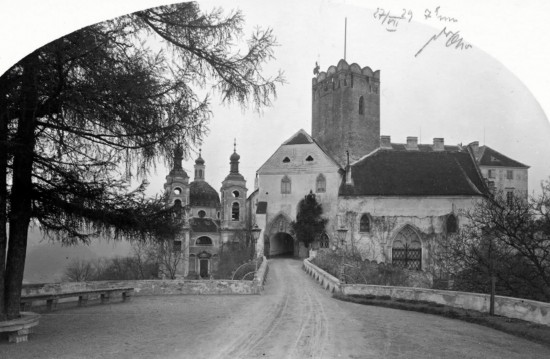 Vstup do Vranovského zámku od západu vede přes vysoký most se zajímavým kruhovým prostranstvím. Až do 90. let 18. století zde stávala samostatně opevněná středověká mostní věž. Pozornost poutá také hranolová (dnes vyhlídková) věž a barokní kaple Nejsvětější trojice (vlevo), dílo významného architekta Fischera z Erlachu, kterou nechali vystavět Althanové i se svou rodovou hrobkou v letech 1698–1700 (srovnávací fotografie z roku 1928 a 2020).