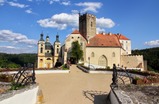 Vstup do Vranovského zámku od západu vede přes vysoký most se zajímavým kruhovým prostranstvím. Až do 90. let 18. století zde stávala samostatně opevněná středověká mostní věž. Pozornost poutá také hranolová (dnes vyhlídková) věž a barokní kaple Nejsvětější trojice (vlevo), dílo významného architekta Fischera z Erlachu, kterou nechali vystavět Althanové i se svou rodovou hrobkou v letech 1698–1700 (srovnávací fotografie z roku 1928 a 2020).